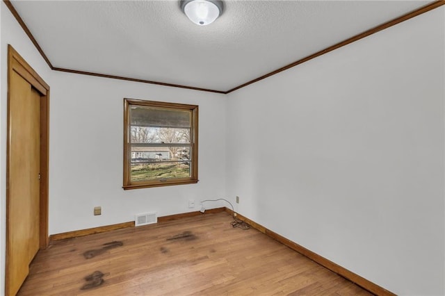 unfurnished bedroom featuring light wood-type flooring, visible vents, a textured ceiling, crown molding, and baseboards