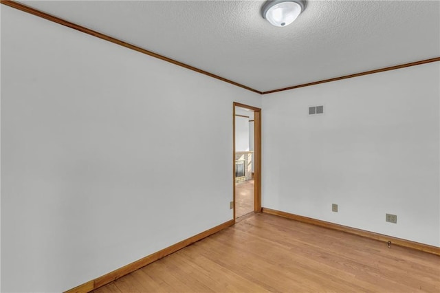 unfurnished room featuring visible vents, ornamental molding, a textured ceiling, light wood-style floors, and baseboards