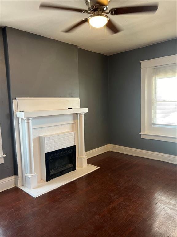 unfurnished living room featuring ceiling fan, a brick fireplace, baseboards, and wood finished floors