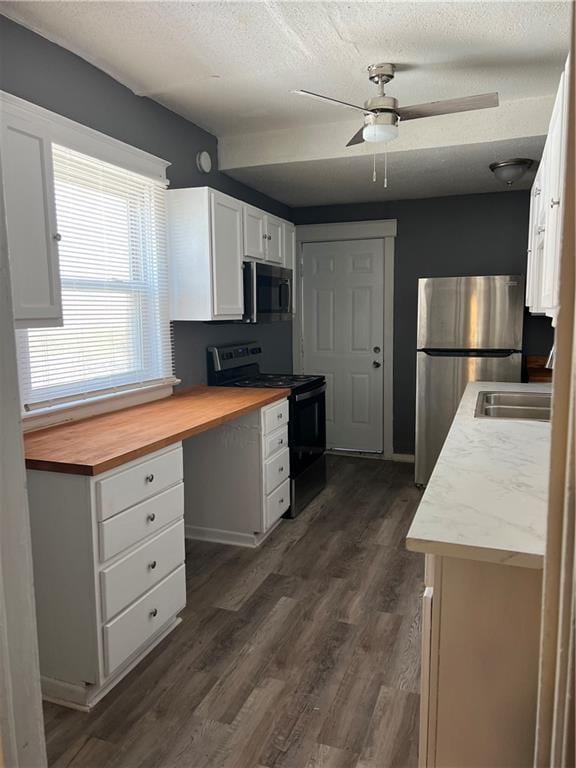 kitchen featuring butcher block countertops, white cabinets, black electric range oven, and freestanding refrigerator