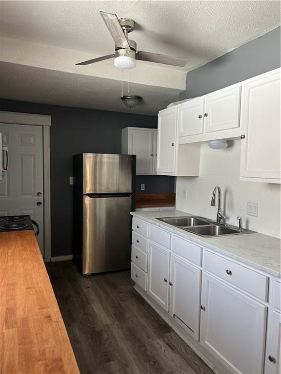 kitchen with a sink, dark wood finished floors, freestanding refrigerator, white cabinets, and wooden counters