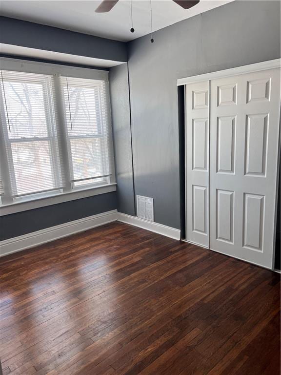 unfurnished bedroom with dark wood-style floors, visible vents, a closet, and baseboards