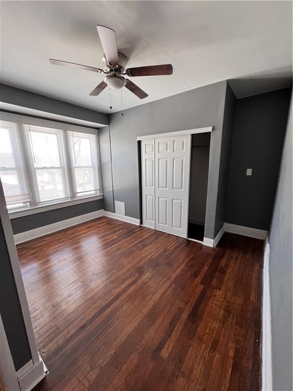 unfurnished bedroom featuring wood finished floors, baseboards, a closet, and ceiling fan