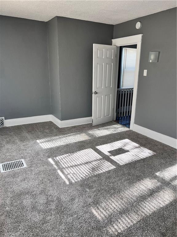 carpeted empty room featuring baseboards, visible vents, and a textured ceiling