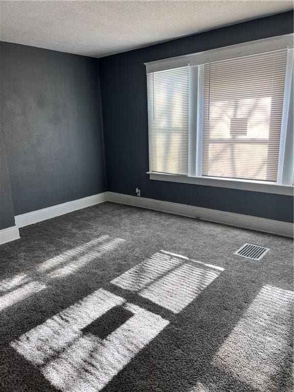 carpeted spare room featuring visible vents, baseboards, and a textured ceiling