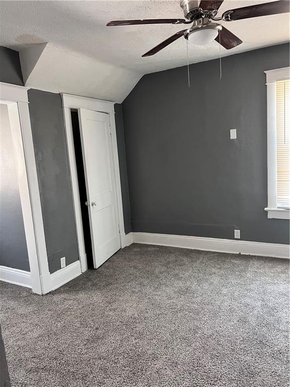 carpeted empty room with vaulted ceiling, a ceiling fan, baseboards, and a textured ceiling