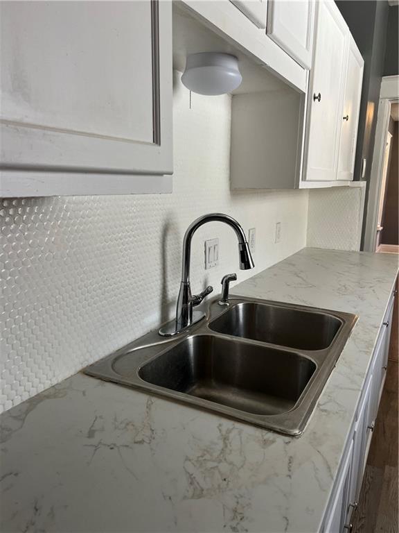 kitchen with light stone counters, backsplash, white cabinetry, and a sink