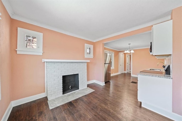 living area featuring dark wood finished floors, an inviting chandelier, a fireplace, crown molding, and baseboards