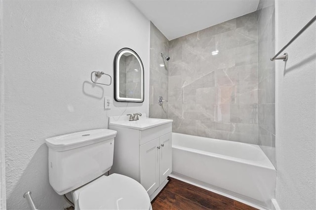 full bath with tub / shower combination, toilet, wood finished floors, a textured wall, and vanity