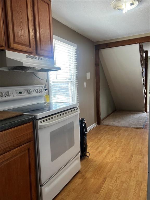 kitchen with under cabinet range hood, a textured ceiling, white range with electric stovetop, light wood-style floors, and brown cabinetry