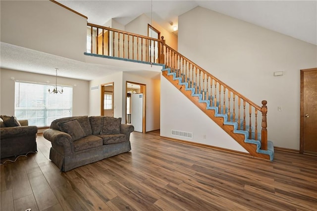 living area with visible vents, a notable chandelier, high vaulted ceiling, wood finished floors, and stairway