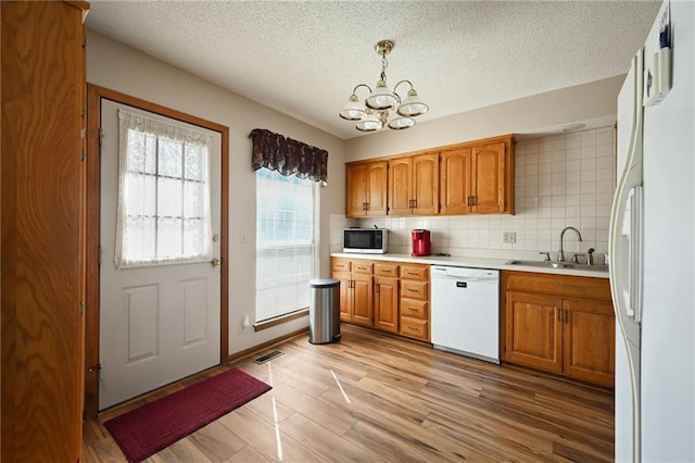 kitchen with visible vents, a notable chandelier, light wood-style flooring, a sink, and white appliances