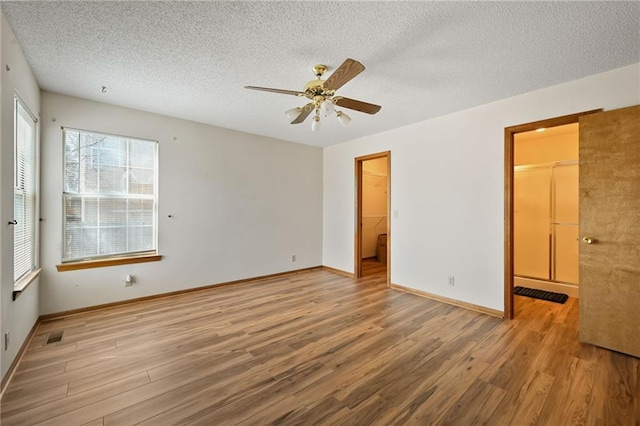 unfurnished bedroom featuring a textured ceiling, wood finished floors, a closet, baseboards, and a spacious closet