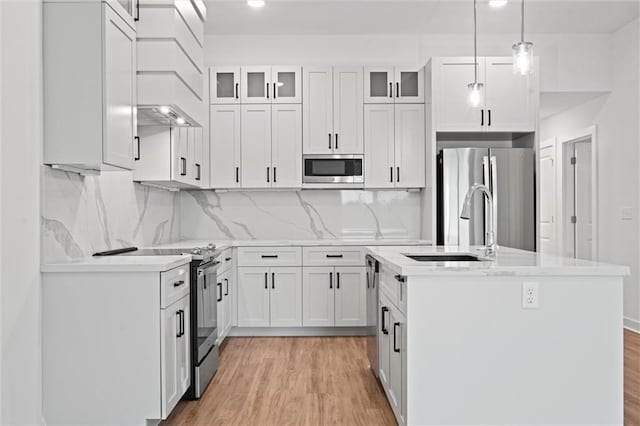 kitchen featuring an island with sink, white cabinets, stainless steel appliances, and light wood-style flooring