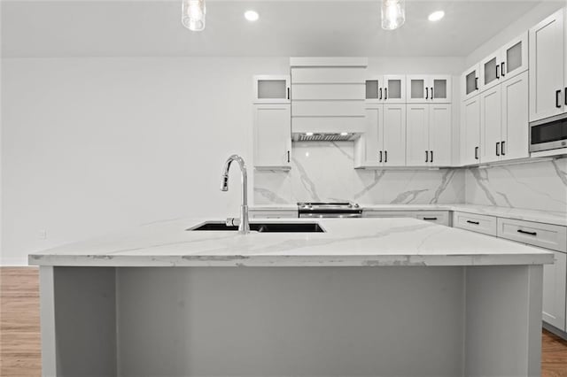 kitchen featuring wood finished floors, an island with sink, a sink, appliances with stainless steel finishes, and backsplash