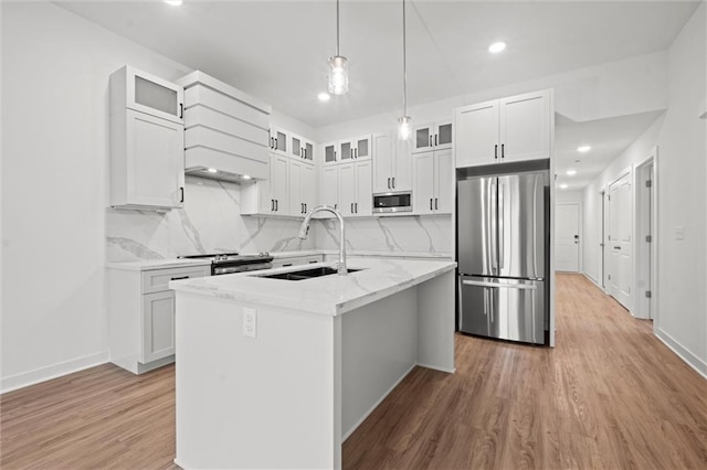 kitchen featuring light wood finished floors, an island with sink, a sink, stainless steel appliances, and white cabinets