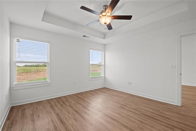 empty room with visible vents, baseboards, a tray ceiling, and wood finished floors