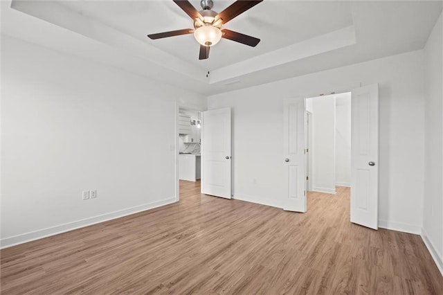 unfurnished bedroom with a tray ceiling, baseboards, light wood-style floors, and a ceiling fan