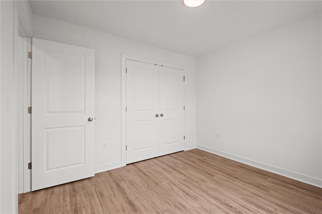 unfurnished bedroom with a closet, baseboards, and light wood finished floors