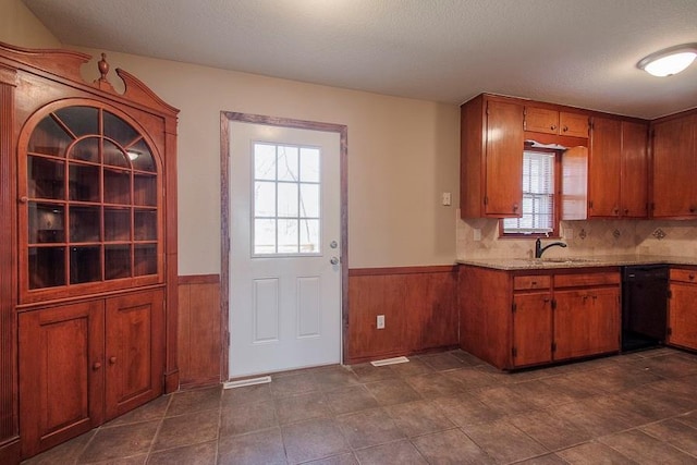 kitchen with brown cabinets, a sink, a textured ceiling, wainscoting, and dishwasher