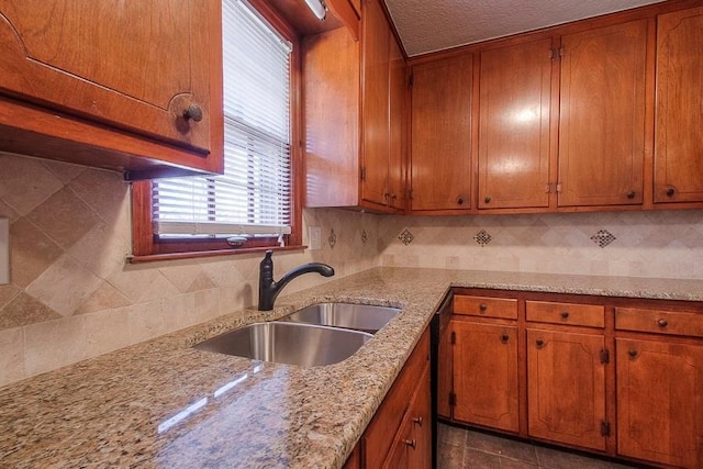 kitchen featuring light stone countertops, brown cabinets, backsplash, and a sink