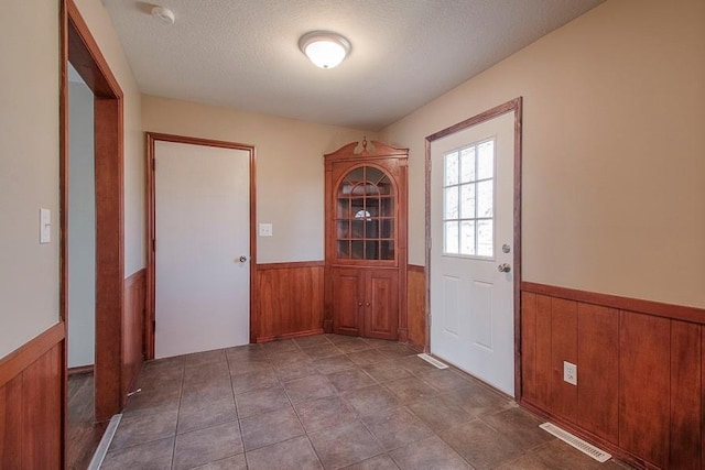 entryway featuring visible vents, wooden walls, a textured ceiling, and wainscoting