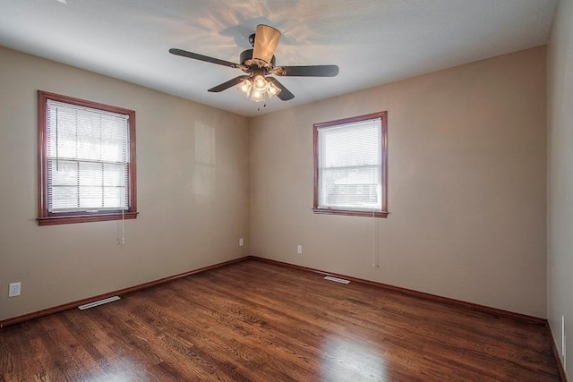 empty room featuring visible vents, plenty of natural light, wood finished floors, and a ceiling fan