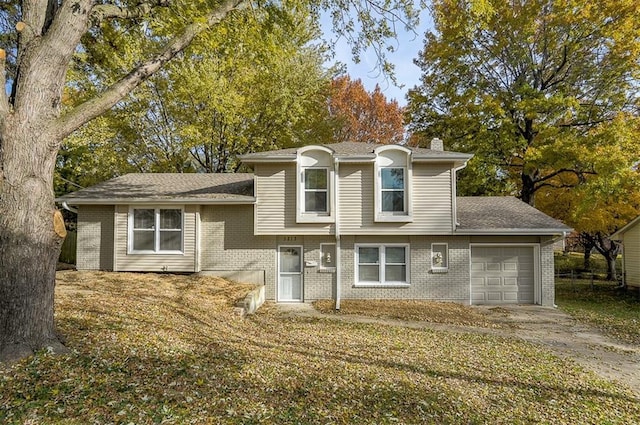 split level home featuring brick siding, concrete driveway, a chimney, and a garage