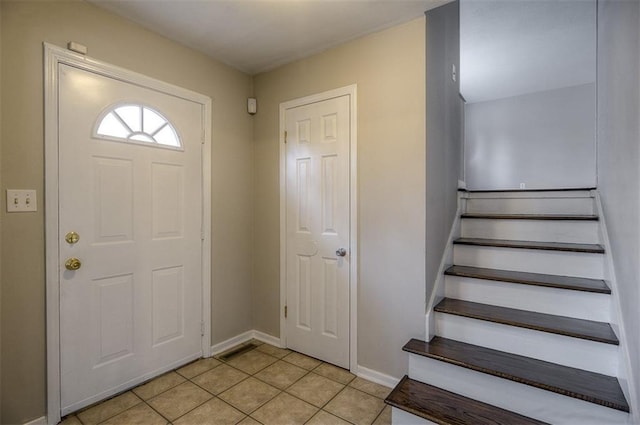 foyer entrance with stairway, light tile patterned flooring, and baseboards