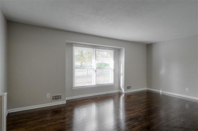 empty room with dark wood finished floors, baseboards, and visible vents