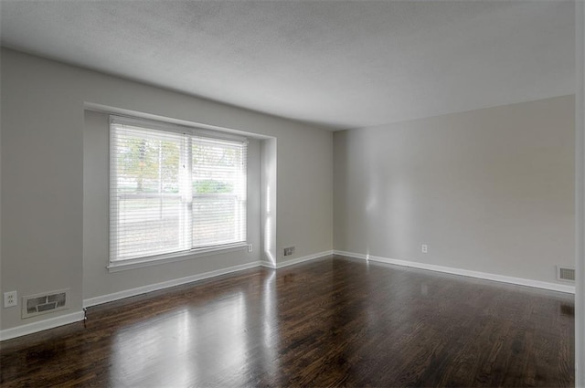 unfurnished room with visible vents, baseboards, and dark wood finished floors