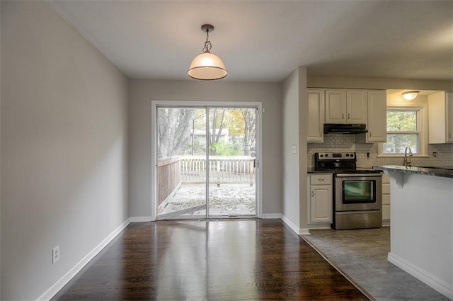 kitchen featuring dark wood-type flooring, electric stove, under cabinet range hood, tasteful backsplash, and baseboards