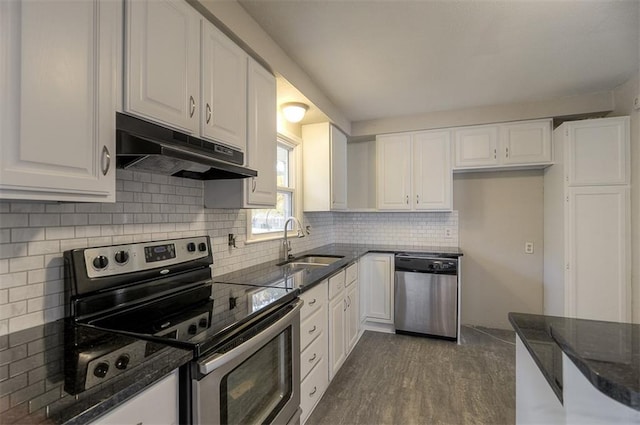 kitchen with dark stone counters, a sink, under cabinet range hood, appliances with stainless steel finishes, and white cabinetry