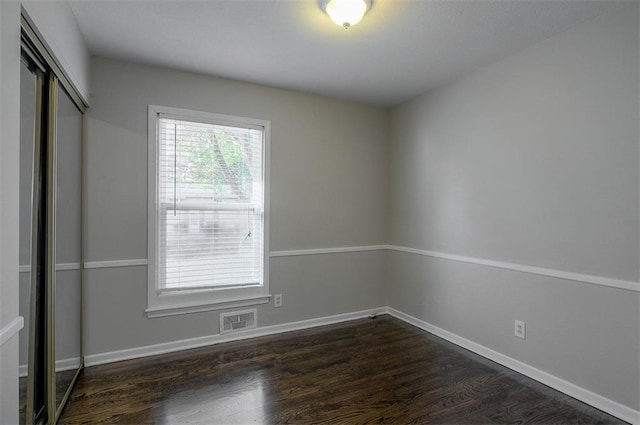 unfurnished bedroom featuring visible vents, baseboards, a closet, and dark wood-style floors