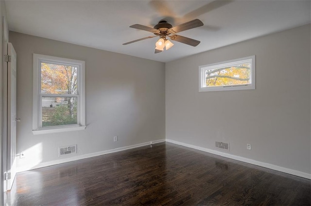 spare room with dark wood-type flooring, visible vents, and a wealth of natural light