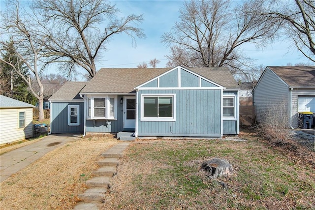 bungalow-style home with driveway, board and batten siding, roof with shingles, and a front lawn