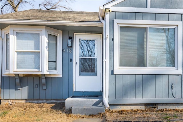 view of exterior entry featuring board and batten siding and a shingled roof