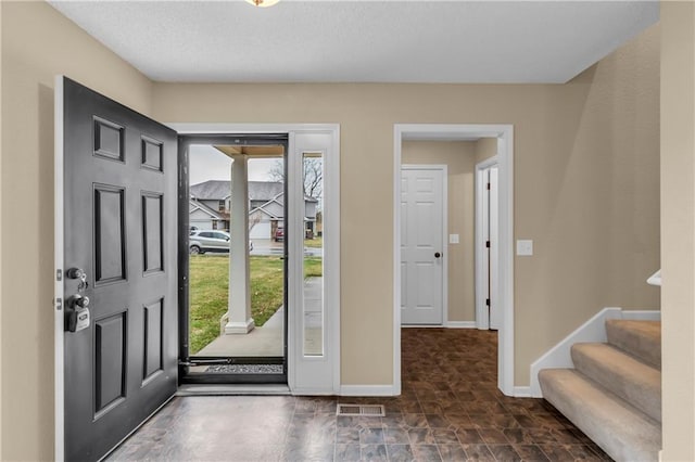 entrance foyer with visible vents, stone finish floor, a textured ceiling, baseboards, and stairs
