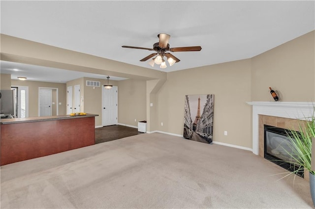 unfurnished living room featuring visible vents, ceiling fan, baseboards, a tiled fireplace, and carpet