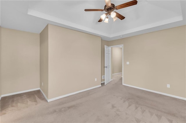 spare room with carpet, a tray ceiling, a ceiling fan, and baseboards