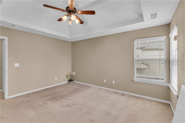 unfurnished room featuring a raised ceiling, baseboards, visible vents, and ceiling fan
