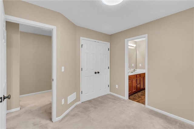 unfurnished bedroom with ensuite bathroom, carpet flooring, baseboards, and a closet