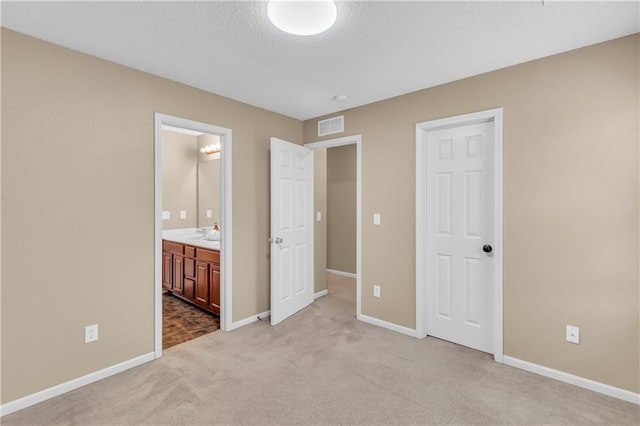 unfurnished bedroom with visible vents, baseboards, carpet, ensuite bathroom, and a textured ceiling