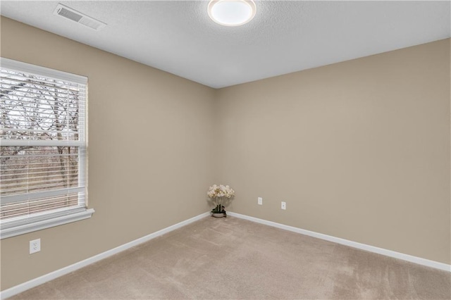 empty room with a textured ceiling, light colored carpet, visible vents, and baseboards