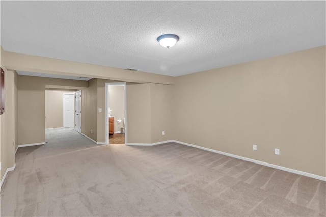 spare room featuring a textured ceiling, visible vents, baseboards, and light carpet