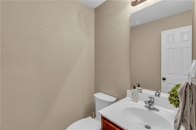 bathroom featuring vanity, toilet, and a textured wall