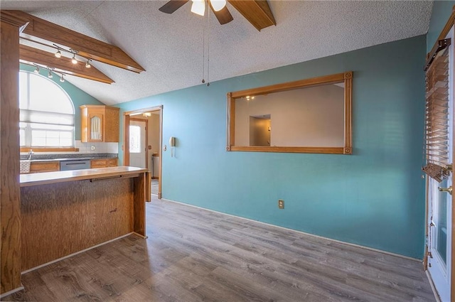 kitchen featuring a ceiling fan, a textured ceiling, wood finished floors, dishwasher, and vaulted ceiling with beams