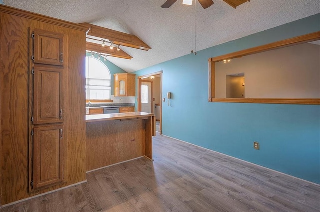 kitchen with brown cabinets, a ceiling fan, a textured ceiling, wood finished floors, and lofted ceiling