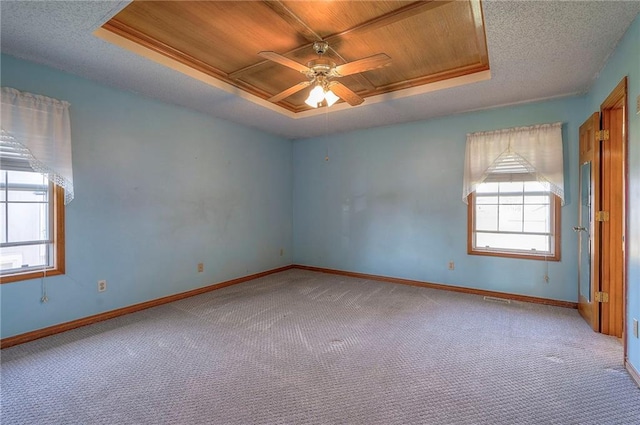 empty room with baseboards, a raised ceiling, carpet, and wood ceiling