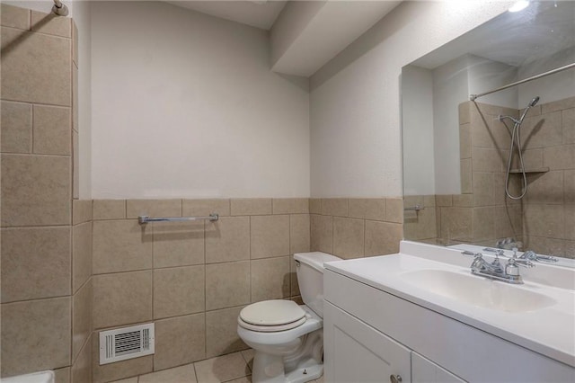 bathroom with tile walls, a tile shower, toilet, vanity, and wainscoting